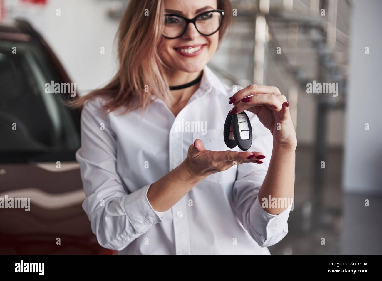 Sei il benvenuto. Donna in eyewear e camicia bianca si trova nei pressi dell' automobile rossa Foto Stock