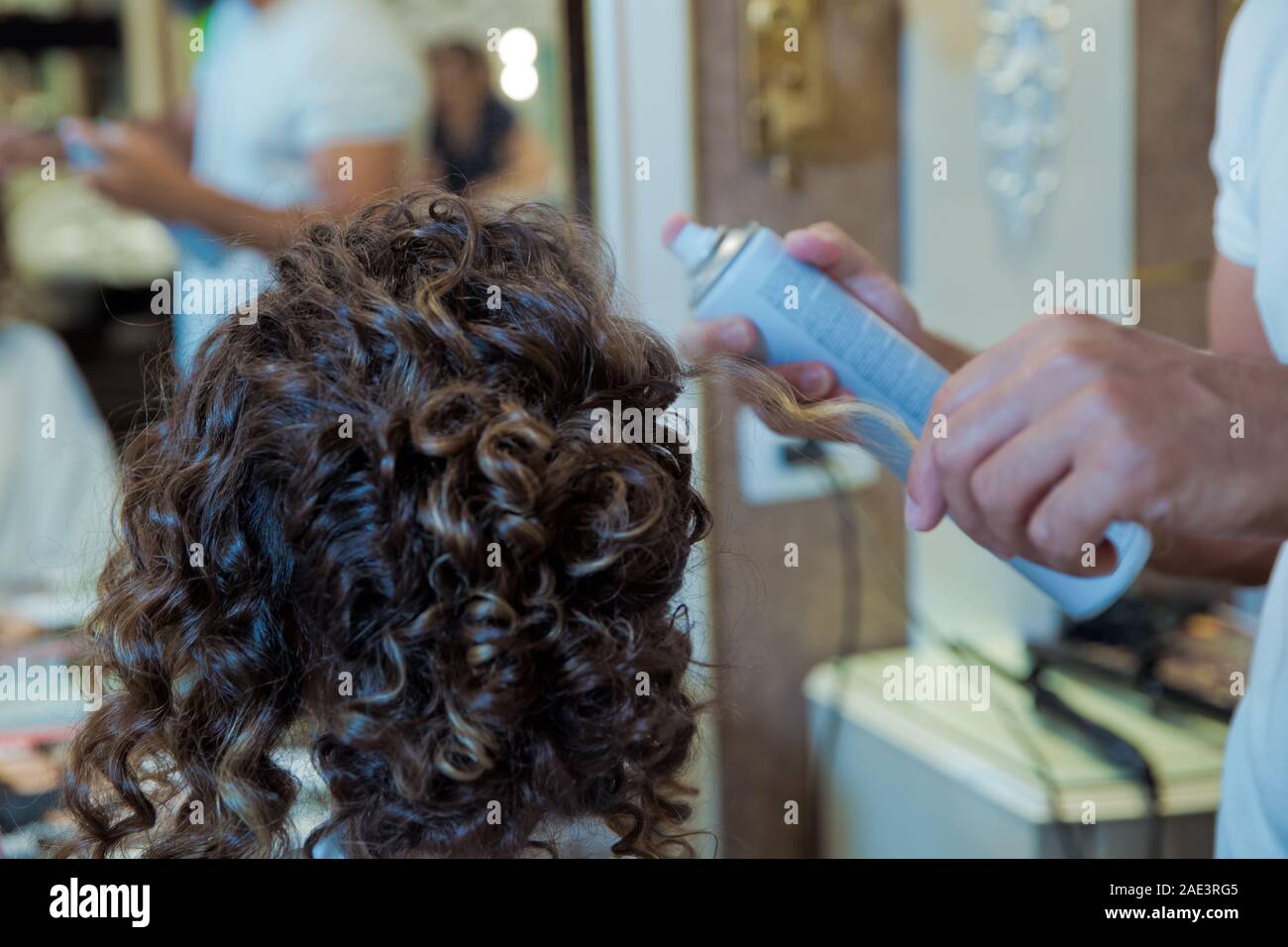 Parrucchiere è utilizzando un spray per capelli sulla donna capelli in un salone di bellezza su uno sfondo di colore marrone. Concetto di parrucchiere professionista studiando.bionda parrucchiere Foto Stock