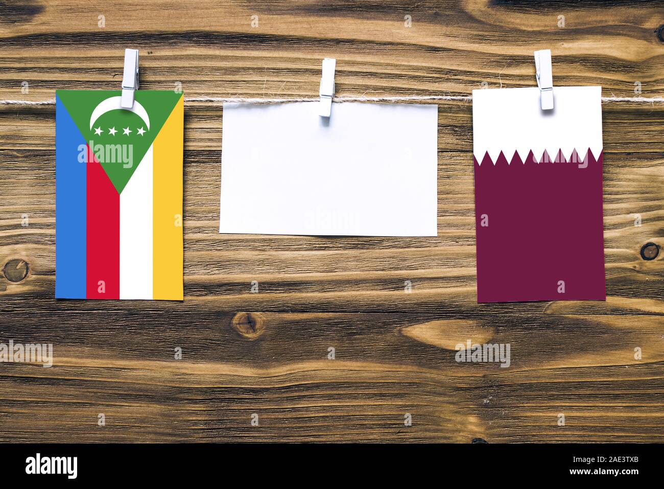 Appendere bandiere delle Comore e Qatar attaccata alla corda con vestiti perni con copia spazio bianco sulla nota carta su sfondo di legno.Le relazioni diplomatiche essere Foto Stock