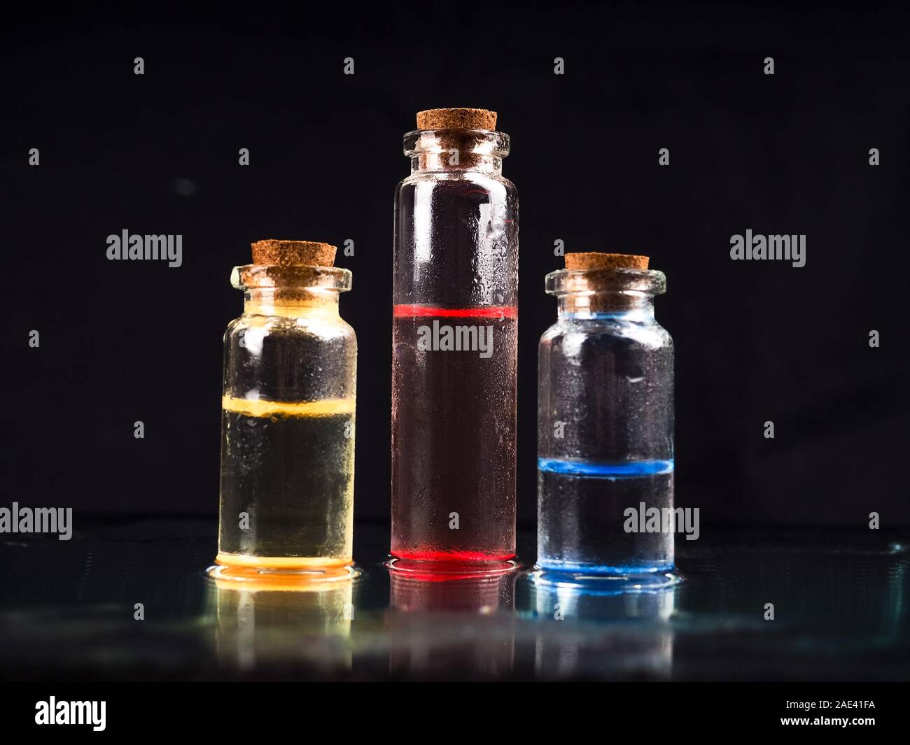 Tre fiale colorate in vetro liquido con fondo nero per la ricerca medica. In un laboratorio chimico fiala di vetro con tappo in sughero in nero. Diversi Foto Stock