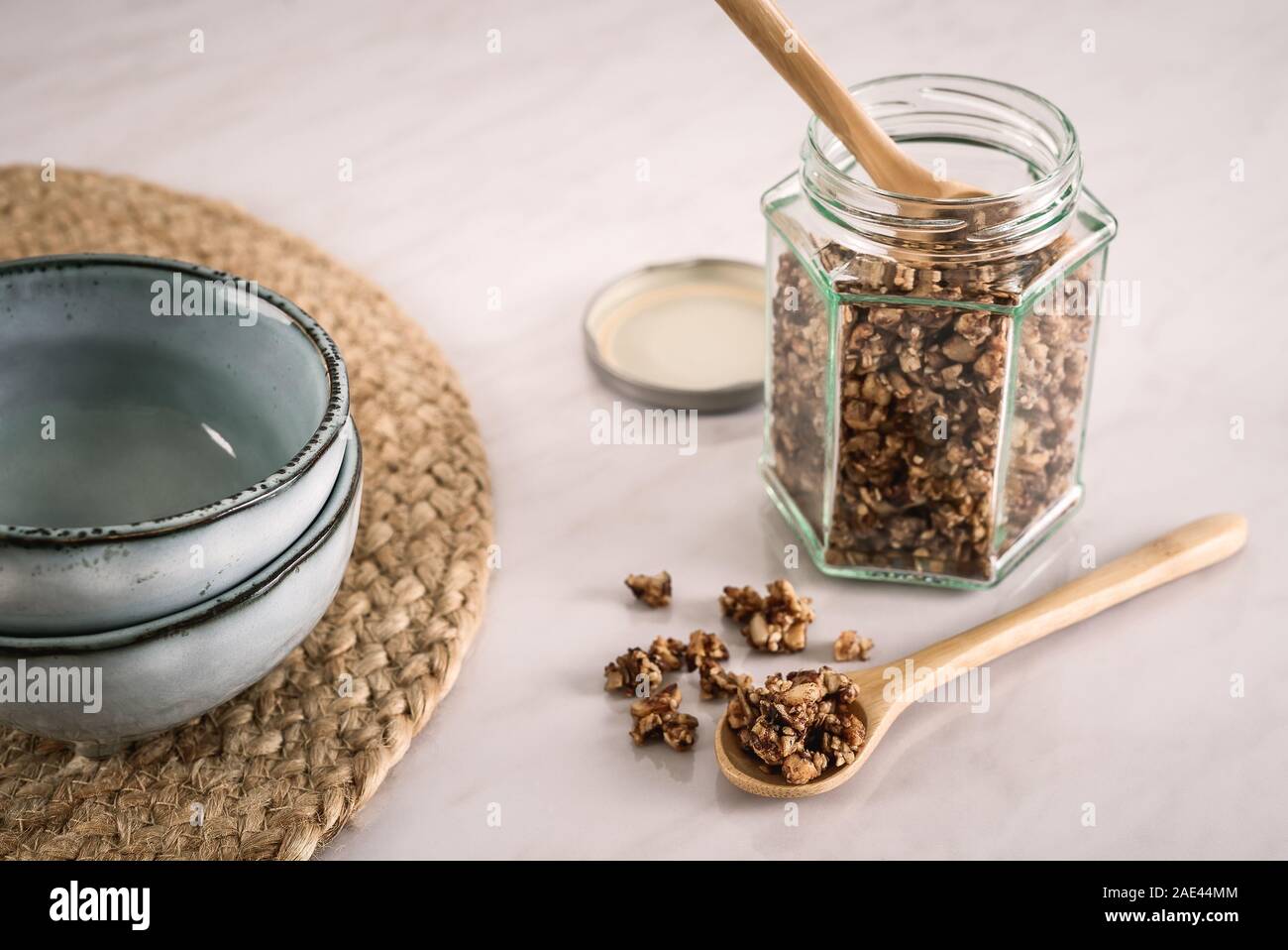 In casa sano e nutriente colazione granola in un vasetto di vetro e il cucchiaio di legno con tazze di ceramica marmo sul tavolo da cucina in fresco. La luce del mattino Foto Stock