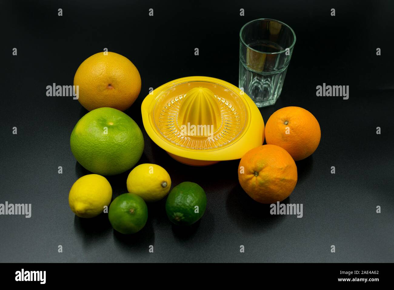 Giallo spremiagrumi con arance, pompelmi, tigli, limoni e bicchiere vuoto su sfondo nero. Foto Stock