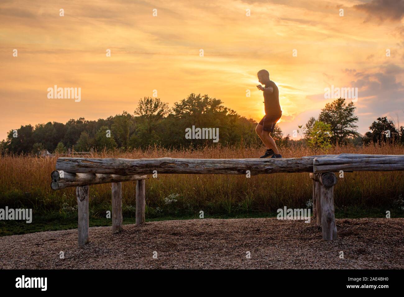 Un uomo cammina attraverso il fascio di equilibrio esterno stagliano tramonto Foto Stock