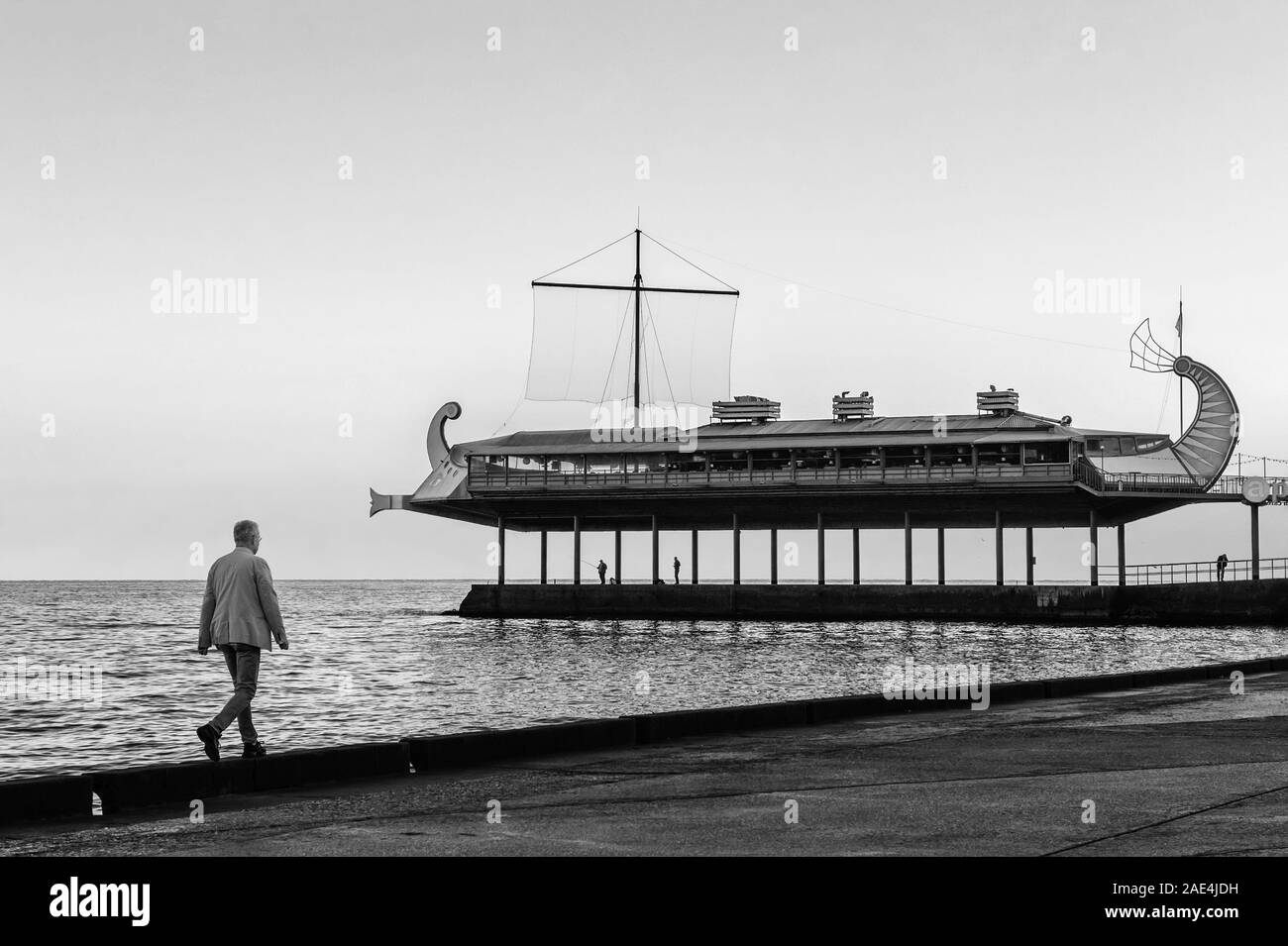 Yalta, Crimea-October 9, 2019: un uomo solitario passeggiate lungo il lungomare godendo di una vista del paesaggio marino al tramonto su un caldo e soleggiato serata d'autunno. Nero a Foto Stock