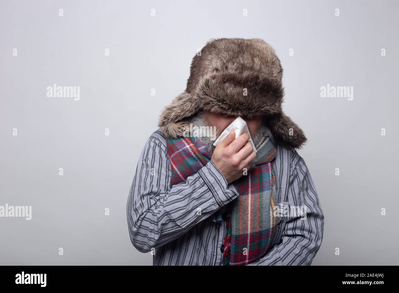 L'uomo è malato e soffiare il naso con un cappello e una sciarpa su sfondo grigio. concetto di salute Foto Stock