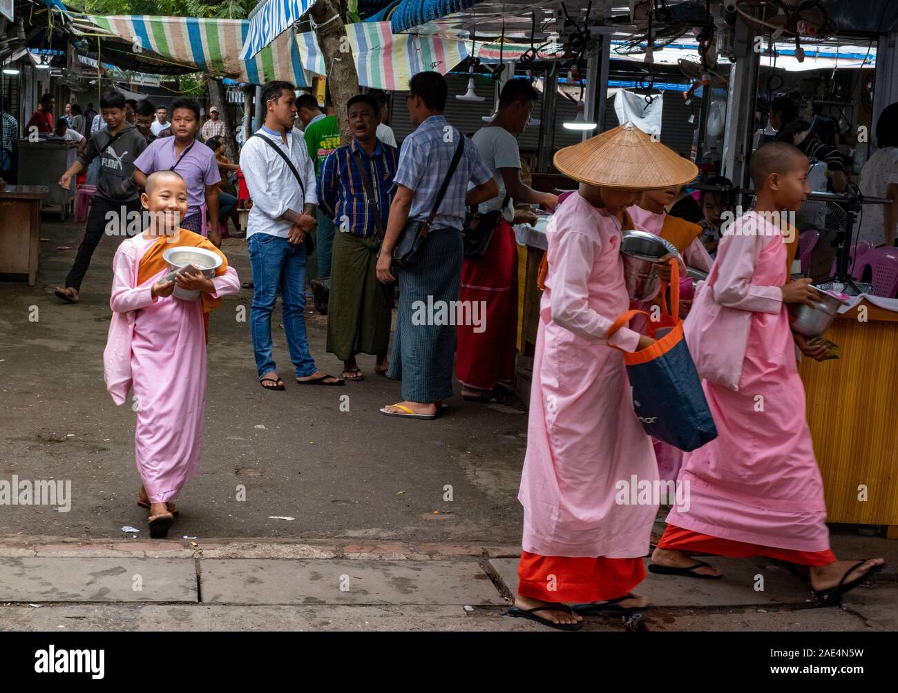 Le monache buddiste passano attraverso un mercato con le loro elemosine bocce in cerca di donazioni durante un giorno santo in Mandalay, Myanmar (Birmania) Foto Stock