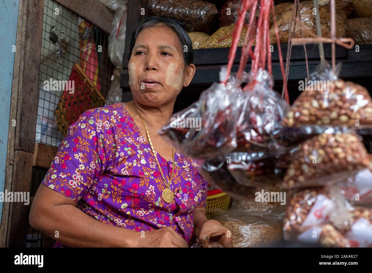 Una donna birmano con polvere di affrontare la vendita di arachidi, peperoni, cereali e cibi essiccati nel mercato ferroviario di Mandalay, Myanmar (Birmania) Foto Stock