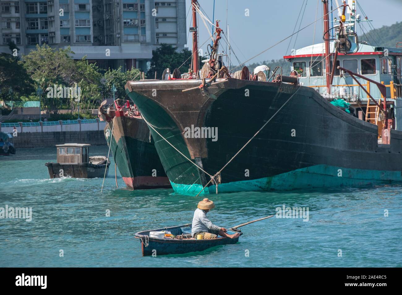 Un pescatore commerciale utilizza una linea a mano su una piccola barca da pesca dell'Isola di Hong Kong con il porto di Aberdeen, circondato da imbarcazioni più grandi Foto Stock