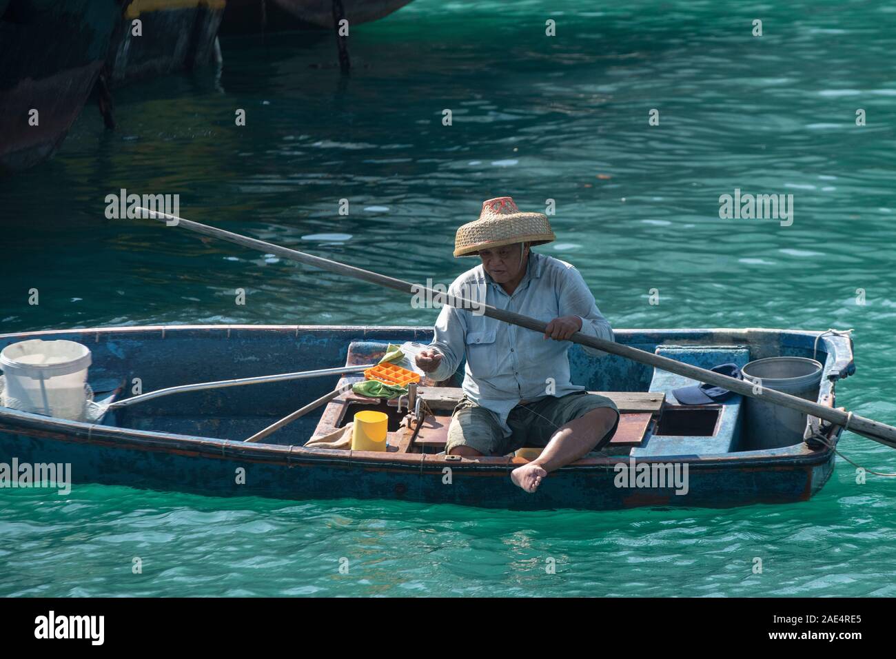 Un pescatore commerciale utilizza una linea a mano su una piccola barca da pesca dell'Isola di Hong Kong con il porto di Aberdeen, circondato da imbarcazioni più grandi Foto Stock