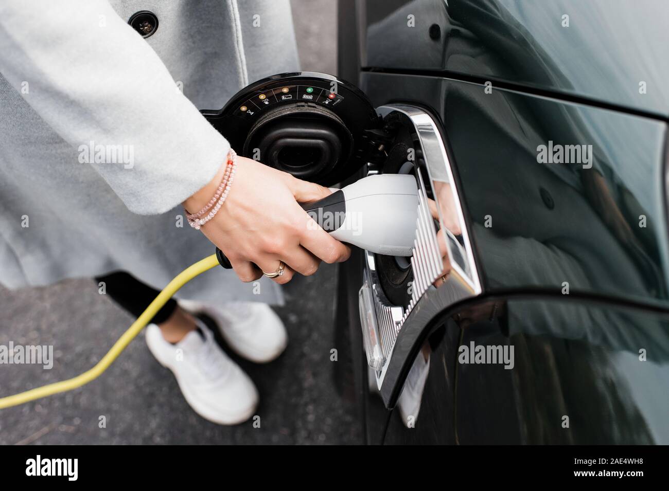 Donna di mano collegando un cavo di ricarica per la sua auto elettrica Foto Stock