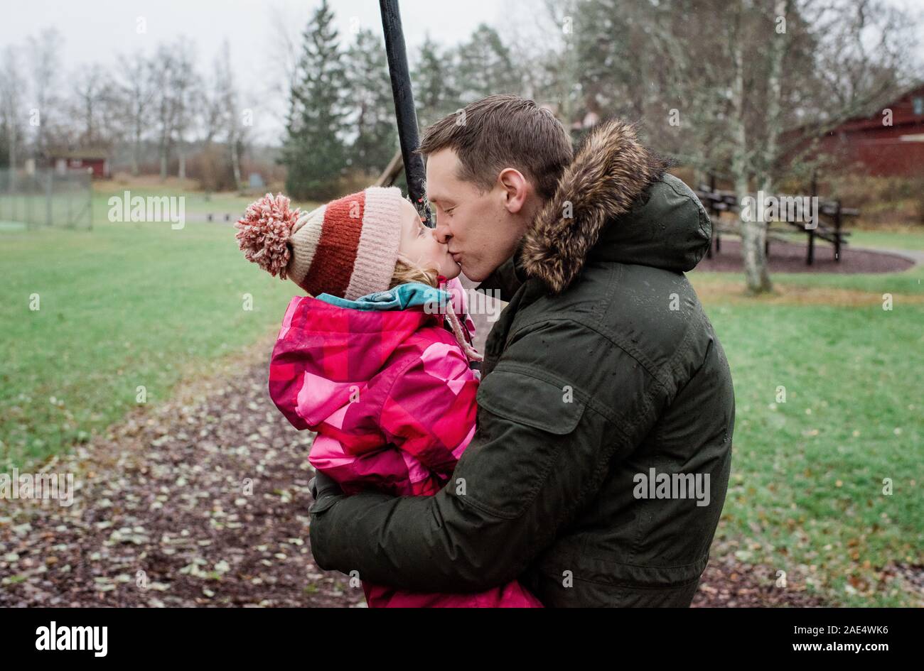 Padre baciare la figlia durante la riproduzione al di fuori in un parco Foto Stock