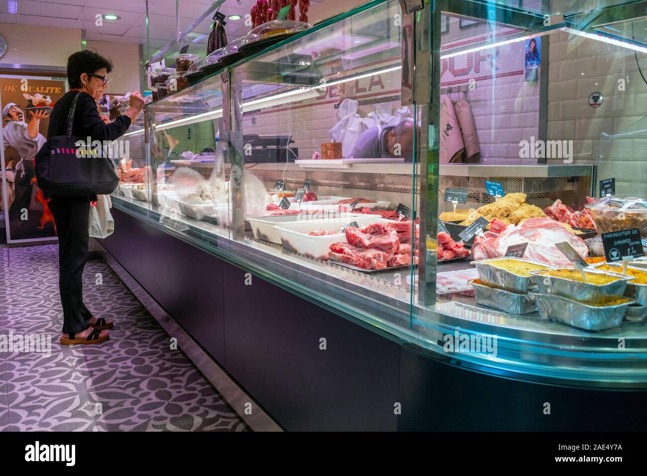 Una femmina di cliente aspetta presso il contatore di una carne macelleria come il cancelliere riempie il suo ordine di Nizza, Francia. Foto Stock