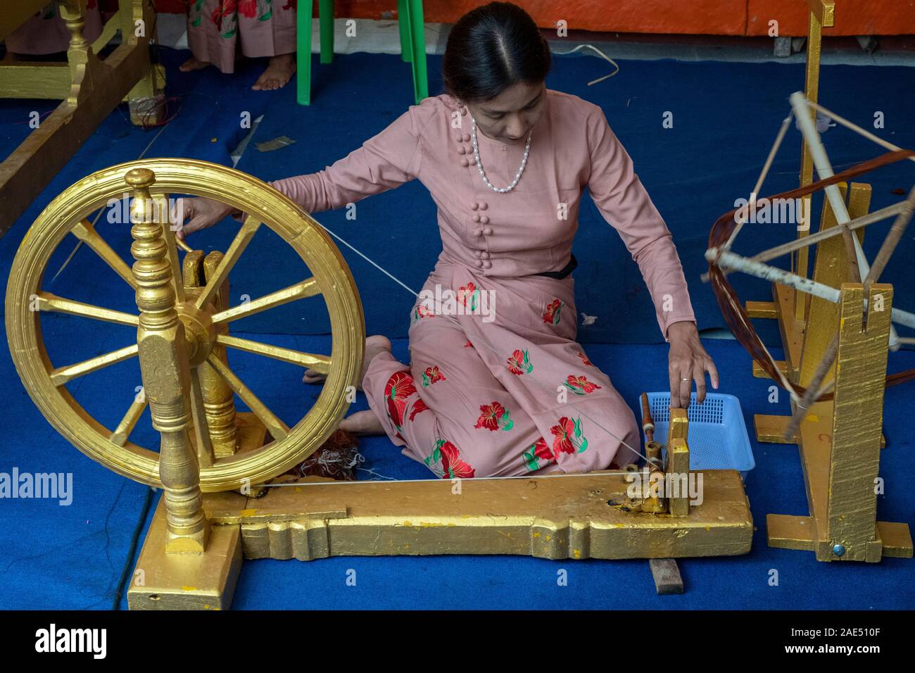 La donna a una ruota di filatura prepara il thread per abiti dello zafferano per i monaci buddisti in un tempio per un buddista annuale vacanza a Mandalay, Myanmar (Birmania) Foto Stock