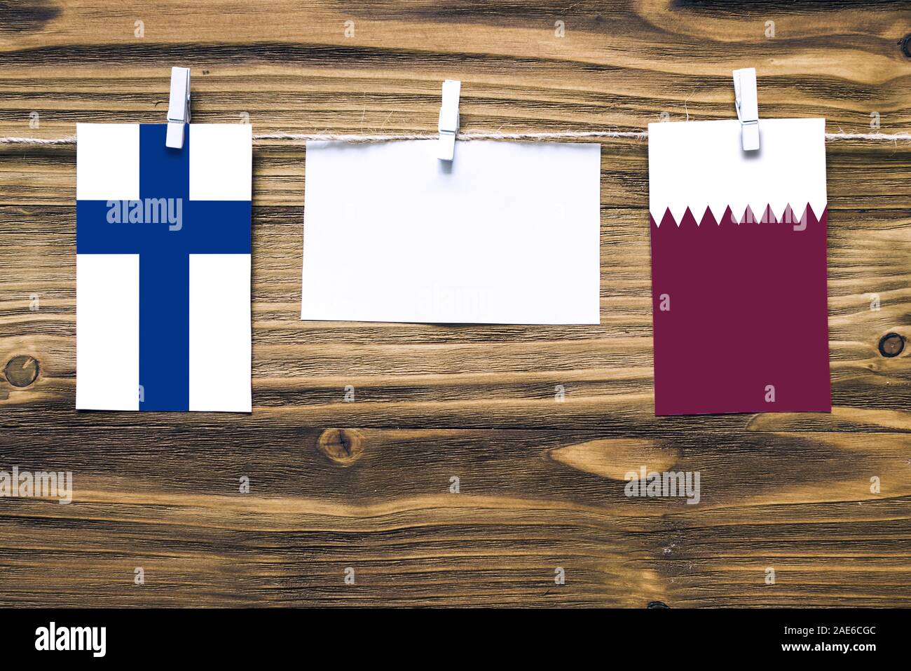 Appendere bandiere della Finlandia e il Qatar attaccata alla corda con vestiti perni con copia spazio bianco sulla nota carta su sfondo di legno.Le relazioni diplomatiche essere Foto Stock