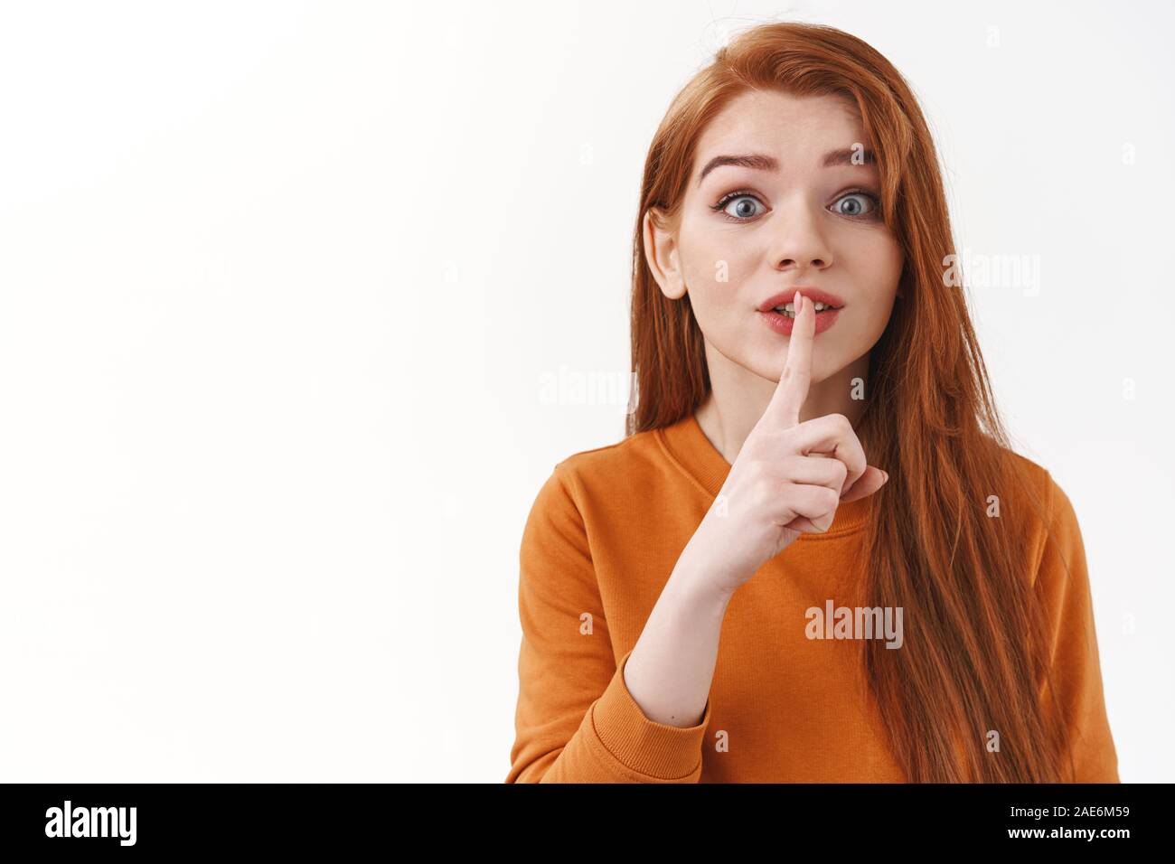 Entusiastico carino e sciocco redhead femmina con lunghi capelli allo zenzero chiedendo a mantenere promite, non dite a nessuno e nasconde il segreto, spettegolare, premuto il dito indice Foto Stock