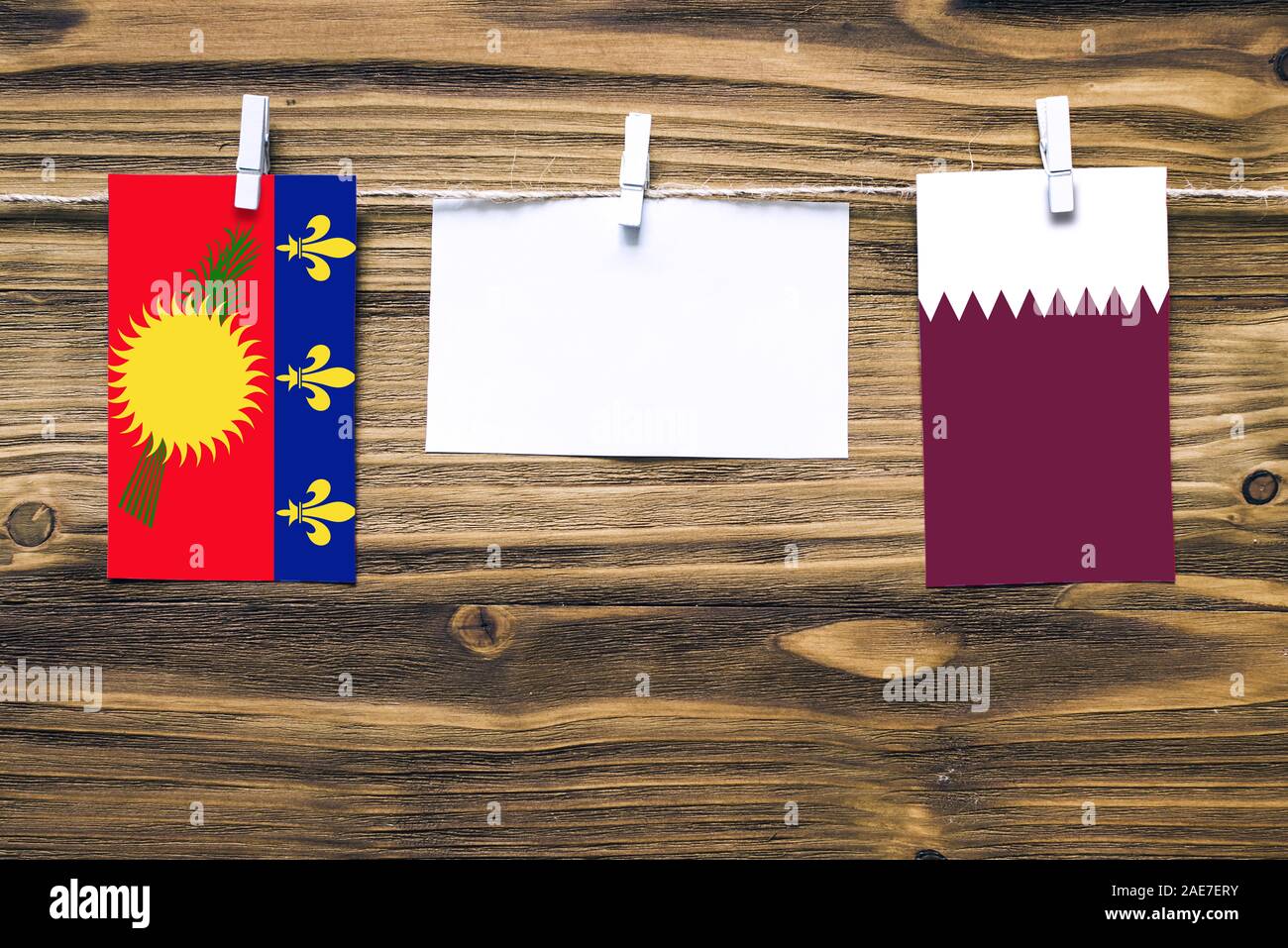 Appendere bandiere della Guadalupa e Qatar attaccata alla corda con vestiti perni con copia spazio bianco sulla nota carta su sfondo di legno.Le relazioni diplomatiche Foto Stock