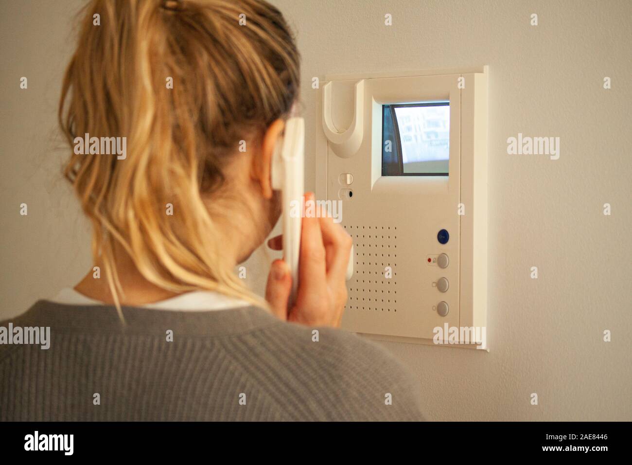 Donna bionda rispondendo a una chiamata a un telefono porta mentre guardando lo schermo sul display CRT. Video citofono attrezzatura. Messa a fuoco selettiva dell'immagine. Foto Stock