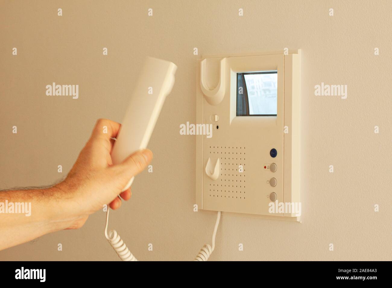 Porta video telefono con immagine su monitor CRT appeso a una parete. Mano che tiene il ricevitore. Video citofono attrezzatura. Messa a fuoco selettiva dell'immagine. Foto Stock