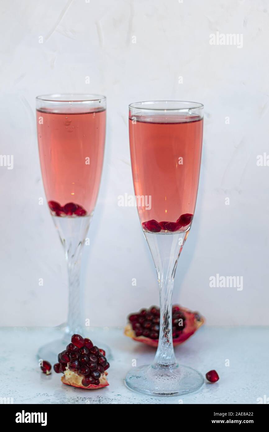 Holiday melograno drink. Vino di colore rosa. Sullo sfondo sono fette di melograno. Sfondo bianco. Champagne. Nuovo anno. Natale. Primo piano. Foto Stock