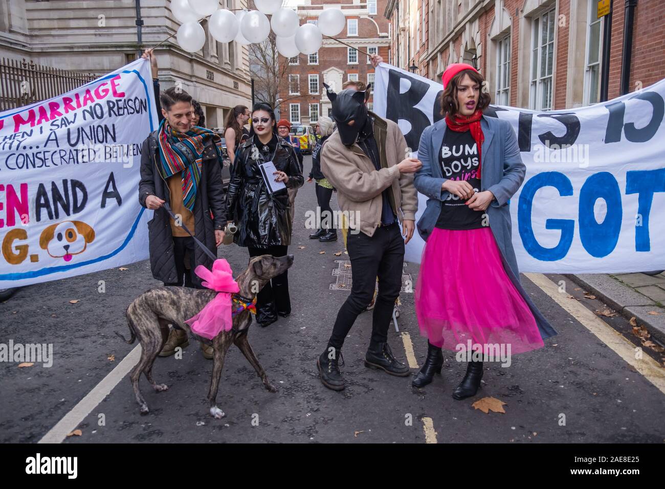 Londra, Regno Unito. Il 7 dicembre 2019. Il cane ha una rosa "abito da sposa". Boris Johnson ha detto: "Se il matrimonio gay è stato OK quindi non ho visto alcun motivo in linea di principio perché un'Unione non dovrebbe essere consacrata tra tre uomini e un cane.' LGBT+ attivisti che hanno preso Boris di etichetta di 'bum boys' celebrare un matrimonio per 3 uomini e un cane fuori Tory HQ la campagna di protesta contro questo e altri suoi omofobi, razzista, ableist e sessista commento prima di marciare per un rally al di fuori di Downing St. Peter Marshall / Alamy Live News Foto Stock