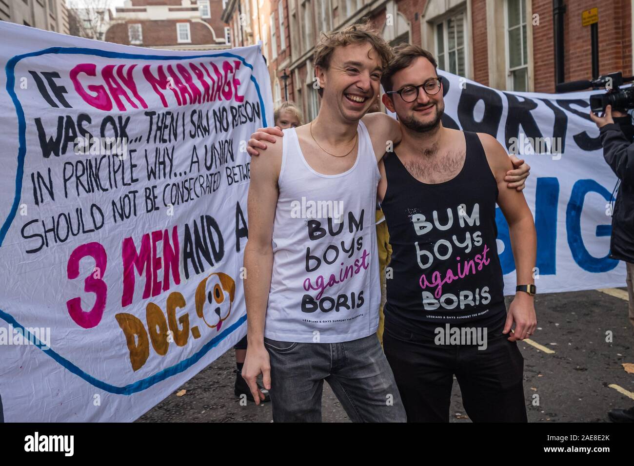 Londra, Regno Unito. Il 7 dicembre 2019. Due uomini pongono di fronte al banner indossando 'Bum Boys contro Boris' canottiere. Boris Johnson ha detto: "Se il matrimonio gay è stato OK quindi non ho visto alcun motivo in linea di principio perché un'Unione non dovrebbe essere consacrata tra tre uomini e un cane.' LGBT+ attivisti che hanno preso Boris di etichetta di 'bum boys' celebrare un matrimonio per 3 uomini e un cane fuori Tory HQ la campagna di protesta contro questo e altri suoi omofobi, razzista, ableist e sessista commento prima di marciare per un rally al di fuori di Downing St. Peter Marshall / Alamy Live News Foto Stock