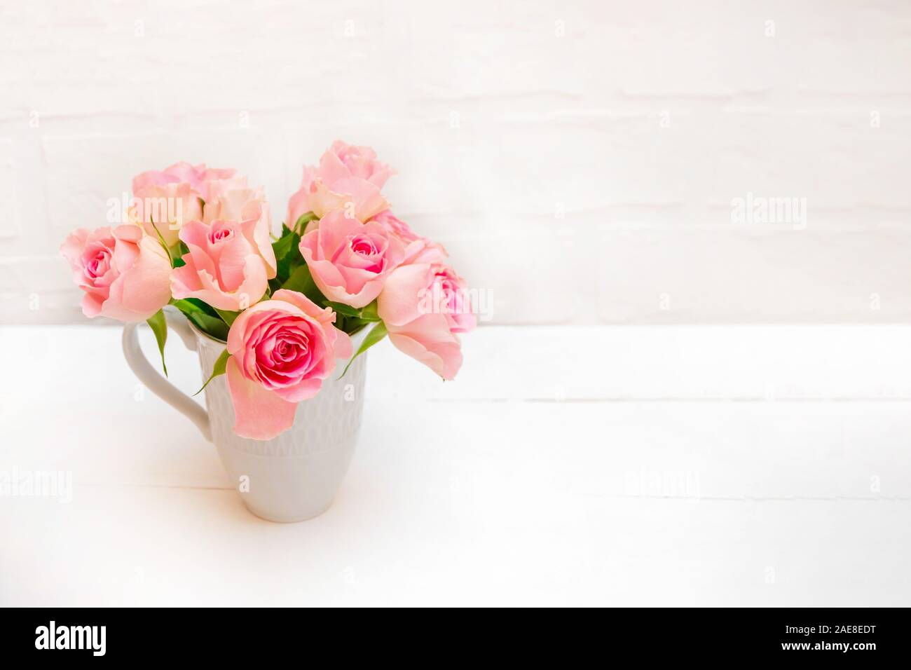 Fresca rosa pastello Rose in un bicchiere di bianco su bianco tavolo in legno Foto Stock
