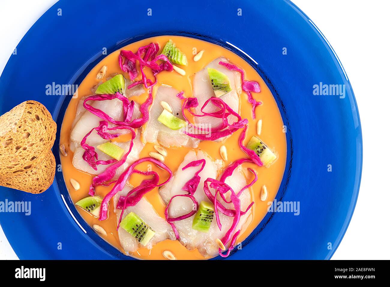 Vista superiore del carpaccio di merluzzo con crema di pomodoro, cavolo rosso, kiwi e Tostate i pinoli in una piastra di colore blu su sfondo bianco. Foto Stock