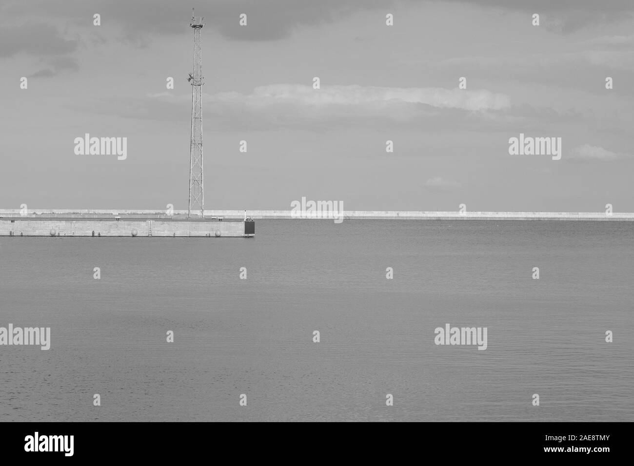 Immagine monocromatica di acqua del porto e i frangiflutti in mezzo con la torre di metallo come sfondo con spazio di copia Foto Stock