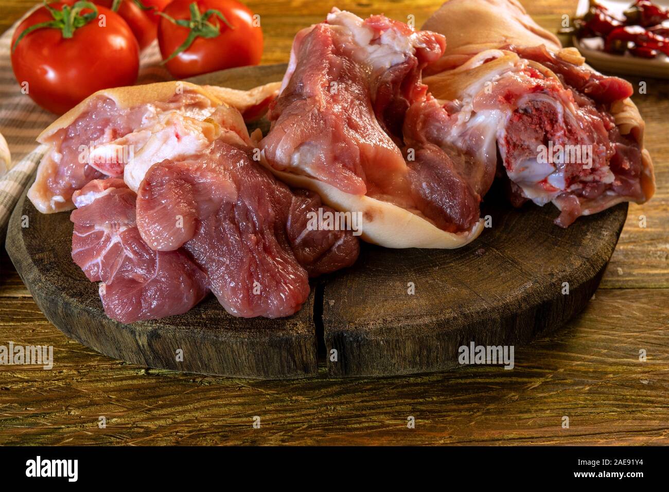 In casa la preparazione del cibo. Materie di maiale tritato оr di articolazione della gamba e pomodori giace sul vecchio dark tagliere di legno. Pronta per la cottura. Messa a fuoco selettiva. Rus Foto Stock