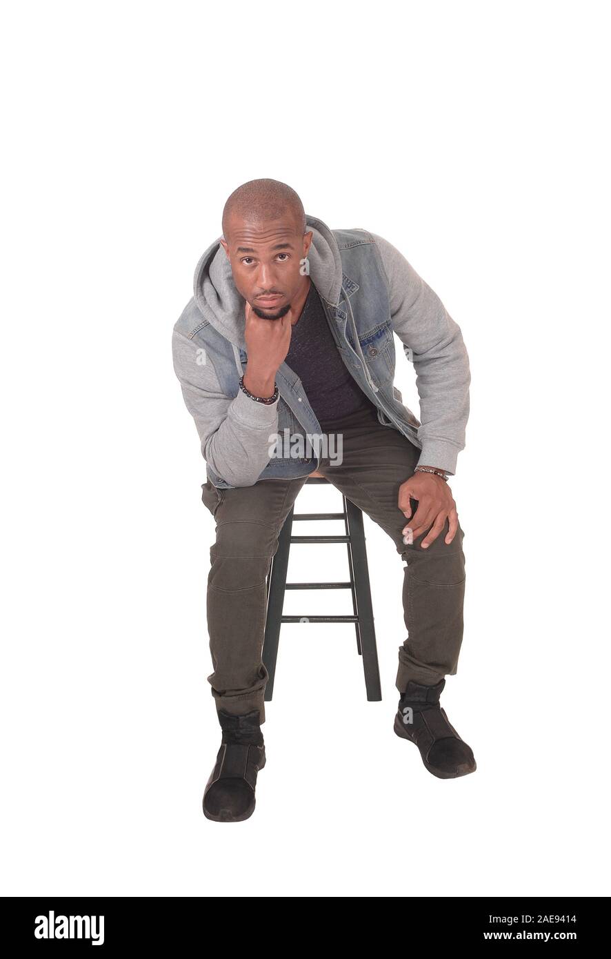 Un giovane bello African American uomo seduto su una sedia con le sue dita sotto il mento, pensando, isolato per sfondo bianco Foto Stock