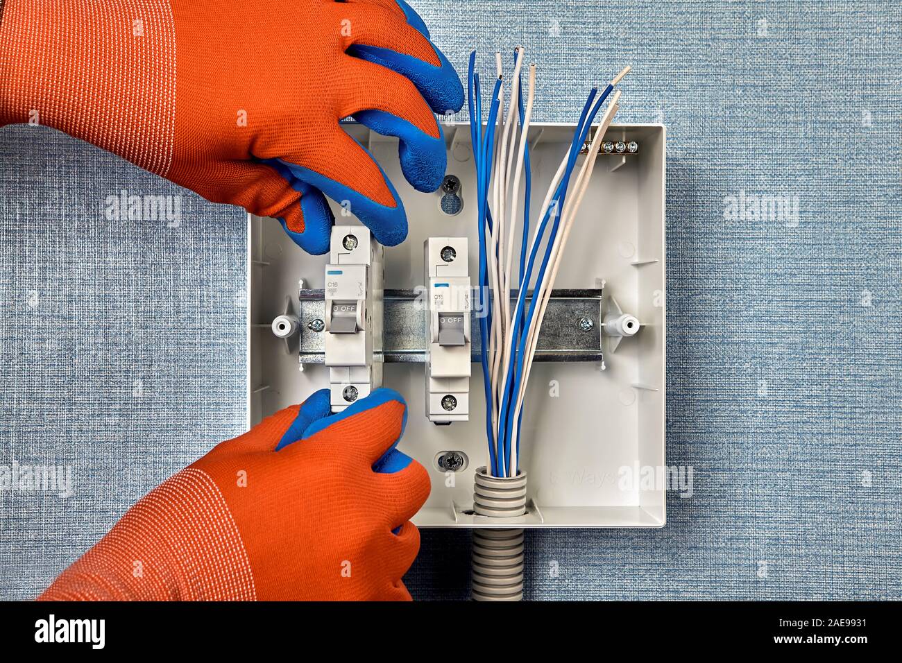 Riparazione e aggiornamento del cablaggio domestico. Un aggiustatore di guanti di protezione installa interruttori di circuito su una guida DIN all'interno di una scatola elettrica. Installazione di Foto Stock