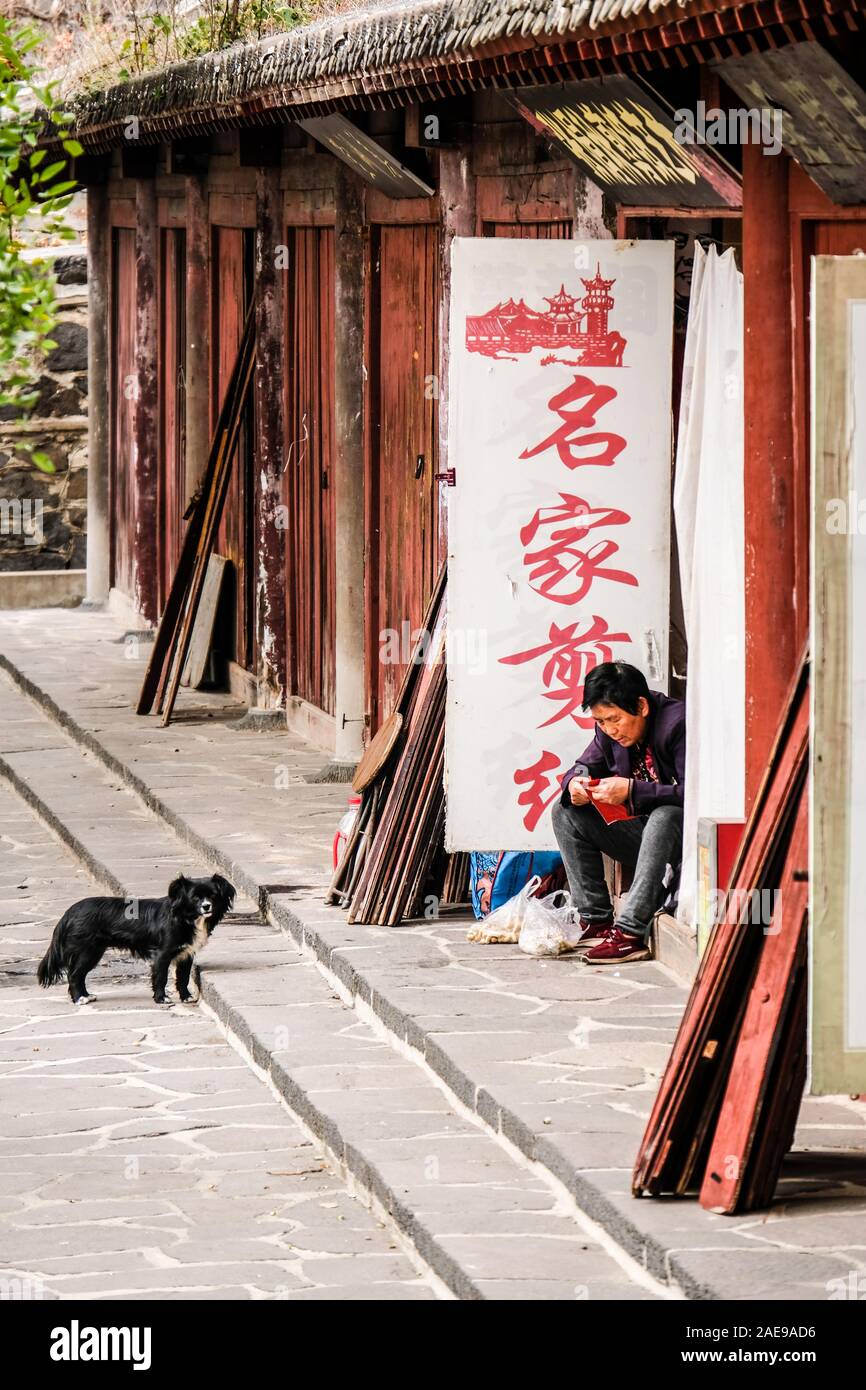 Un venditore di carta cinese unico seduto al suo negozio con un piccolo cane Foto Stock