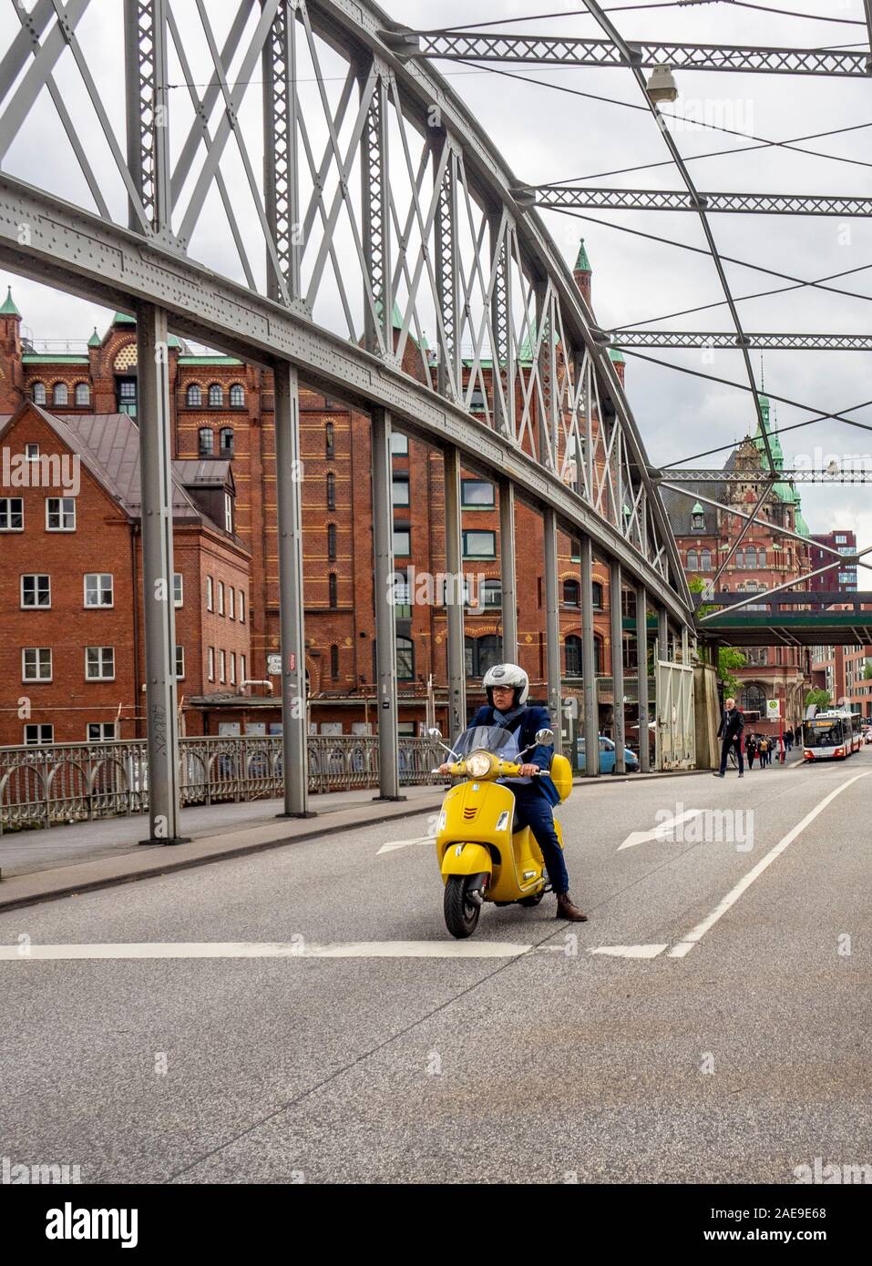 Uomo su uno scooter giallo sul ponte di Kornhaus ponte traliccio in acciaio che collega Altstadt al distretto magazzino Speicherstadt sopra il canale Zoll Amburgo Germania. Foto Stock