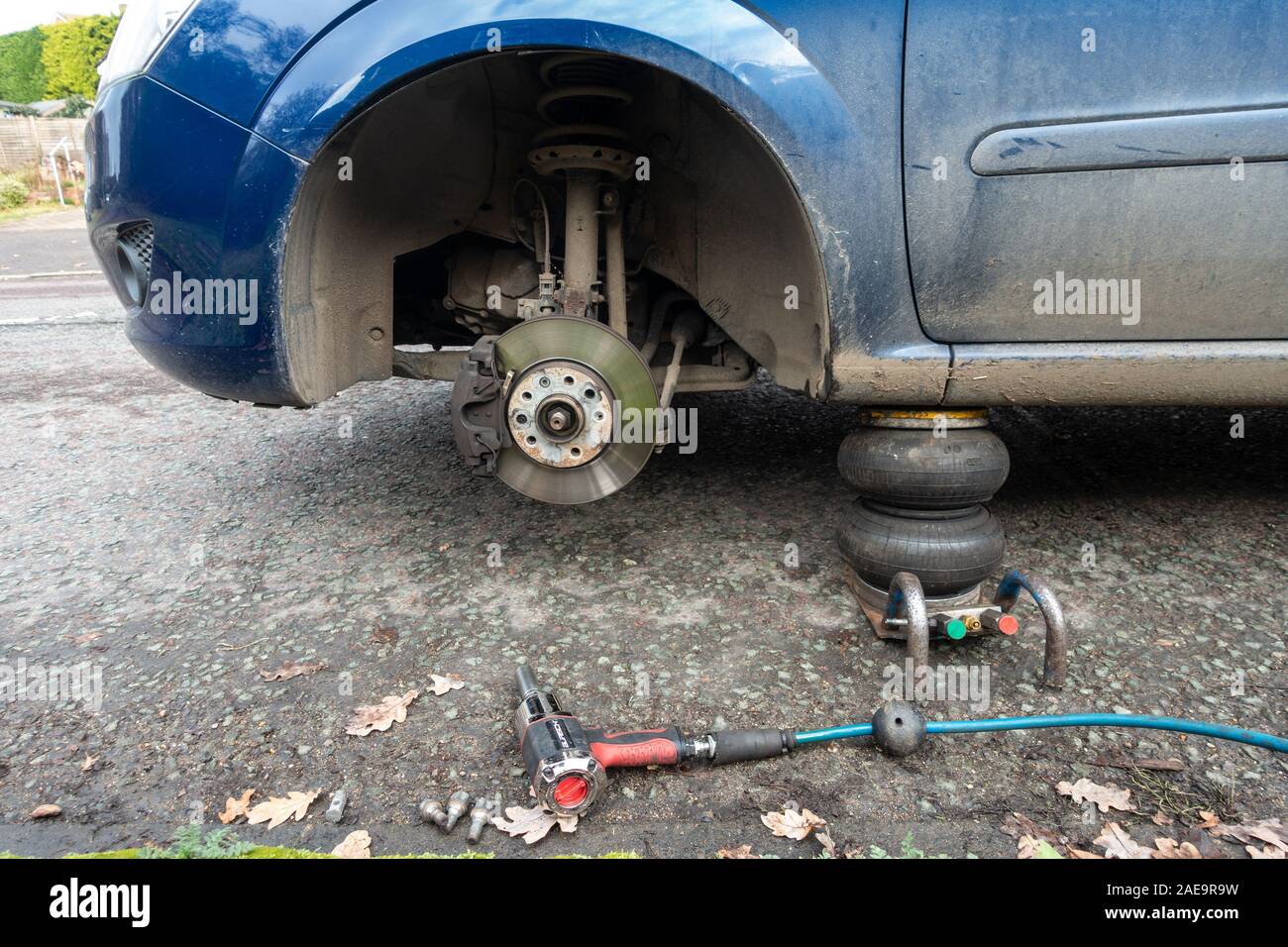Una vettura sollevato sul ciglio della strada con una delle ruote anteriori mancanti in una foratura viene riparato da un mobile per la riparazione dei pneumatici azienda. Foto Stock