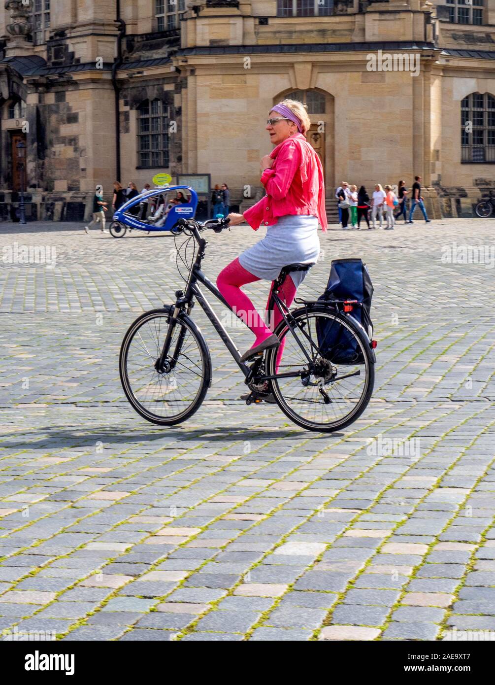 Donna caucasica anziana che indossa giacca rosa e calze in bicicletta in bicicletta attraverso Platz Neumarkt Newmarket Altstadt Dresden Sassonia Germania. Foto Stock