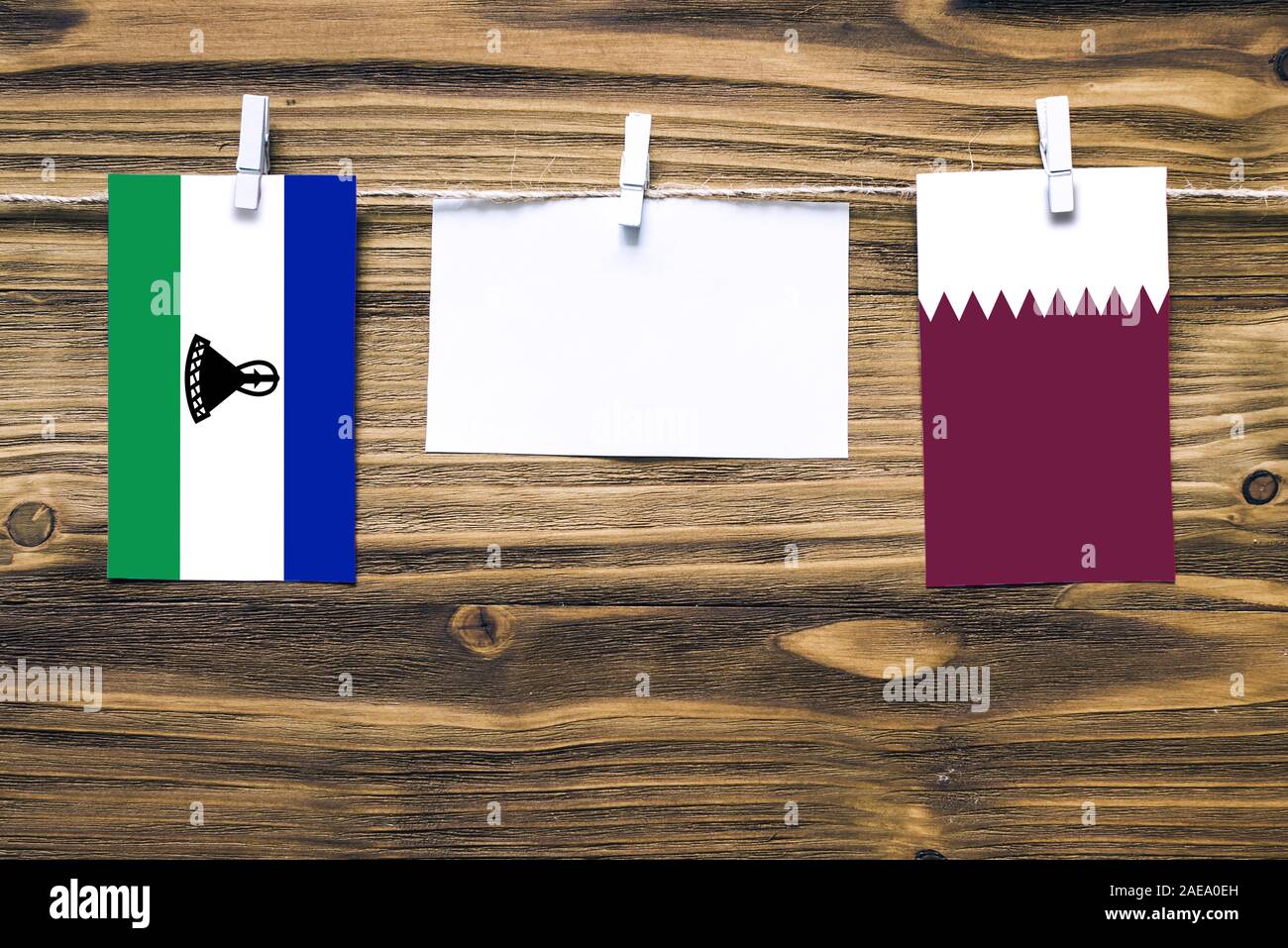 Appendere bandiere del Lesotho e Qatar attaccata alla corda con vestiti perni con copia spazio bianco sulla nota carta su sfondo di legno.Le relazioni diplomatiche essere Foto Stock