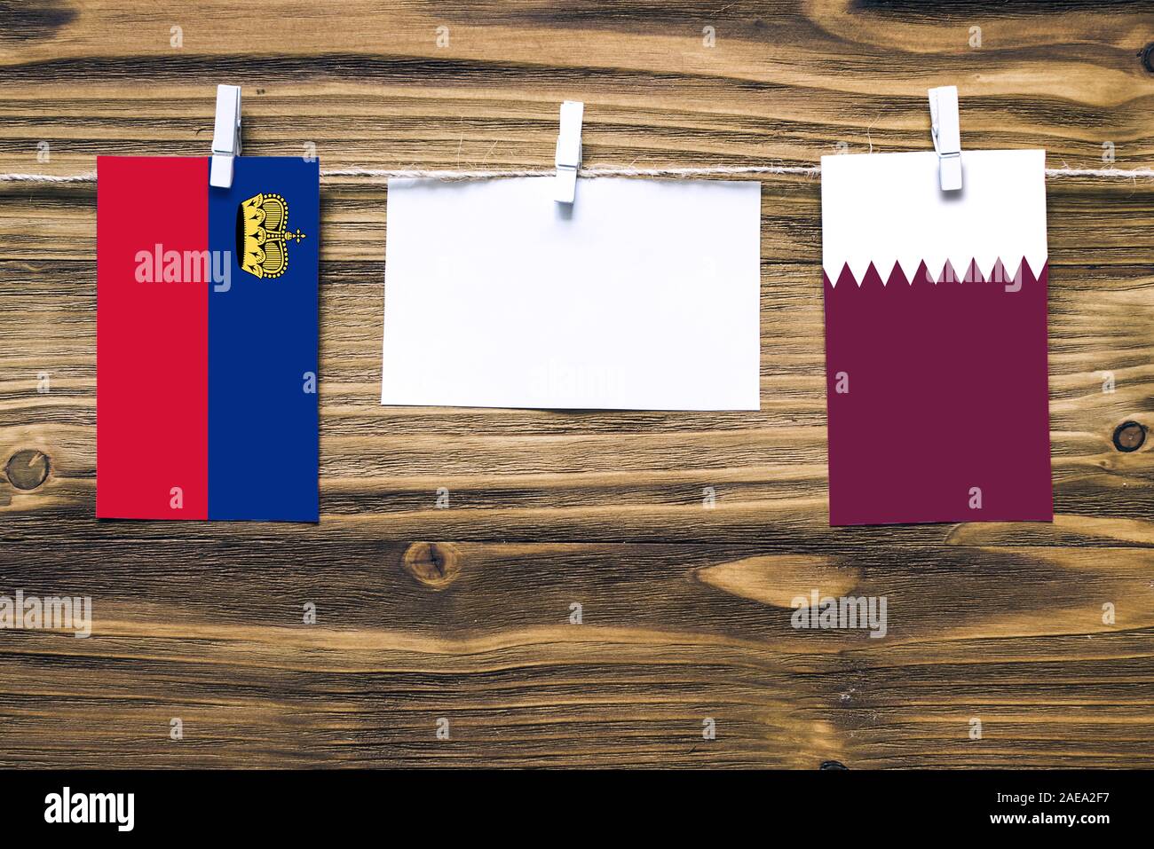 Appendere bandiere di Liechtenstein e Qatar attaccata alla corda con vestiti perni con copia spazio bianco sulla nota carta su sfondo di legno.Diplomatic relativi Foto Stock