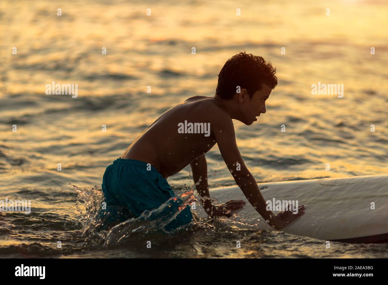 Stanco di un ragazzo con un rack di surf in un costume da bagno per imparare le diapositive sulle onde Foto Stock