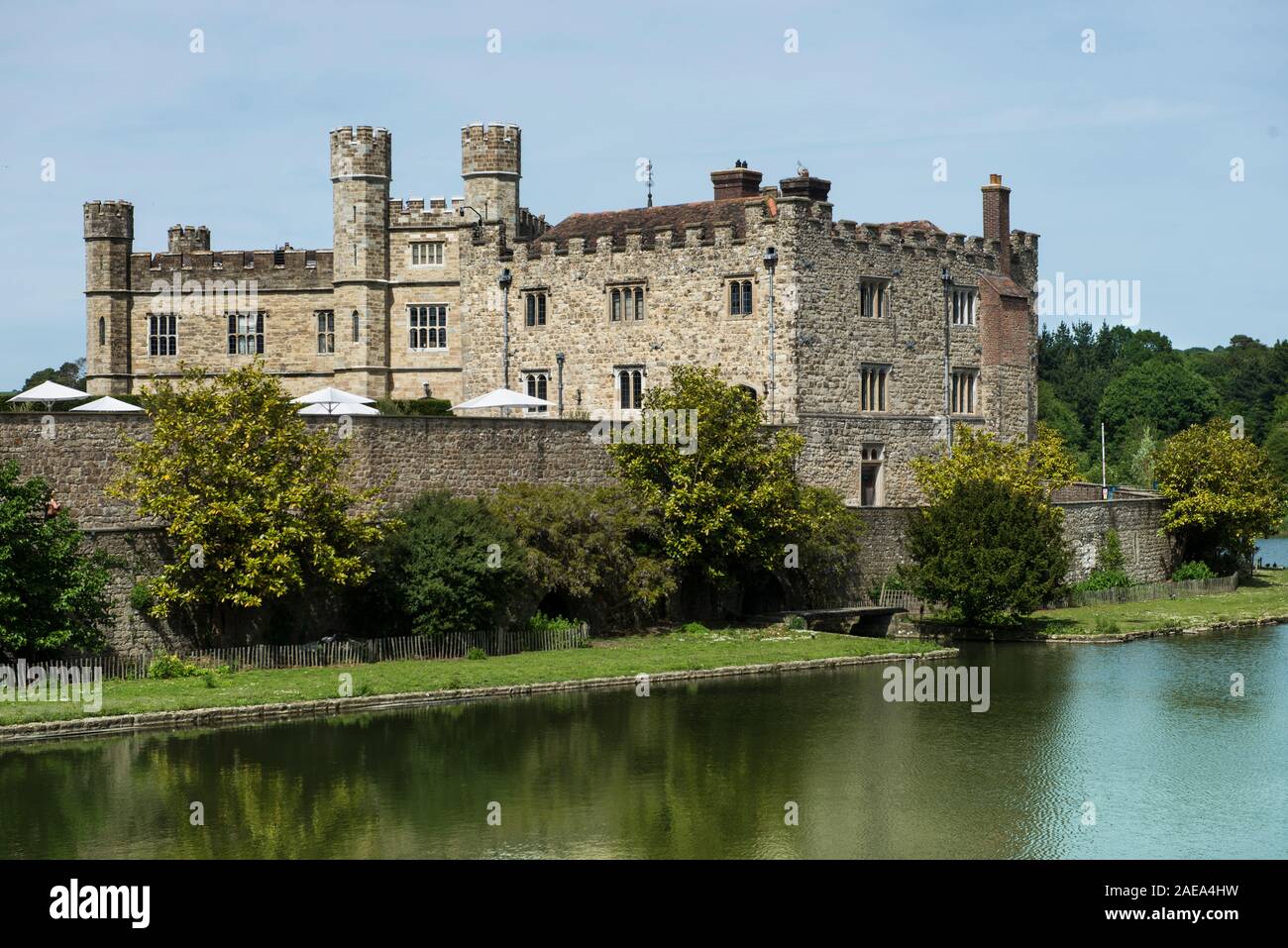 Vista lago del Castello di Leeds castello principale riflesso nel fossato del castello. Antico muro di pietra oscurando tavoli all aperto con il bianco pantina parasole ombrelli. Foto Stock