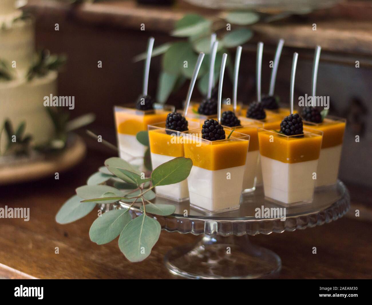 Giallo e Bianco dessert di gel con more decorate con rami di eucalipto e con cucchiai in loro Foto Stock