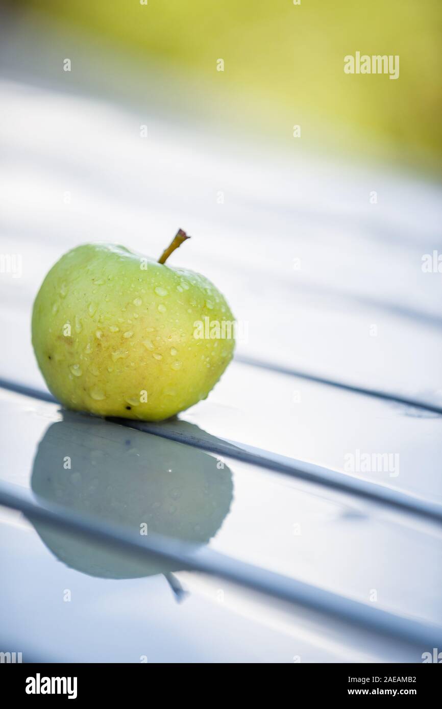 Primo piano di un verde mela organico sul bagnato al tavolo da giardino. Bella riflessione di Apple sul tavolo. Apple dopo la pioggia di estate. Foto Stock