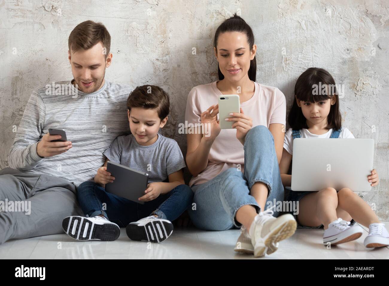 La famiglia felice con bambini seduti sul pavimento mediante dispositivo moderno. Foto Stock