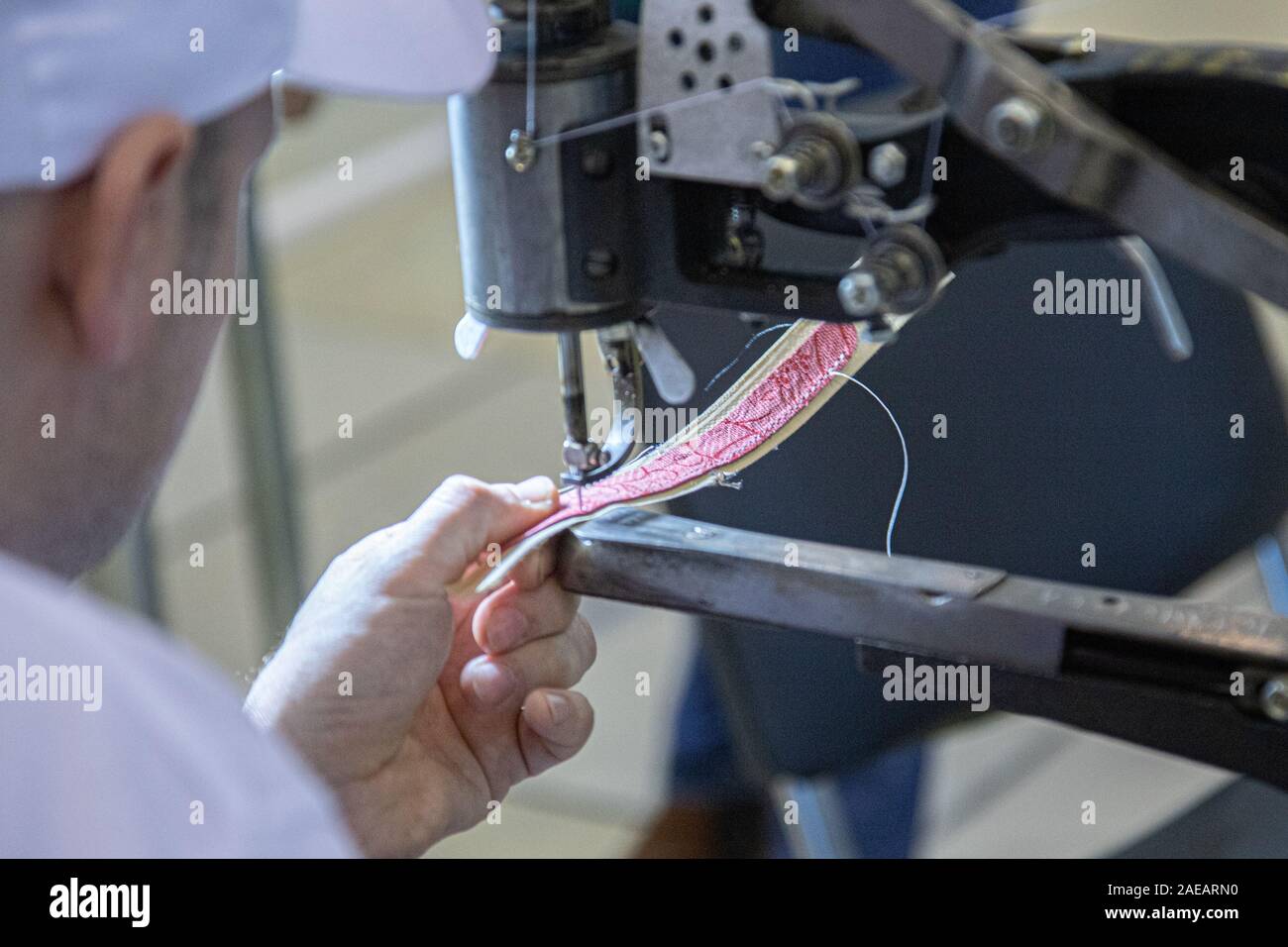 Le mani di un vecchio e un lavoratore con esperienza nella calzatura artigianali industria, eseguendo operazioni di cucitura su un pezzo di pelle vera, su un cuoio cucito machi Foto Stock