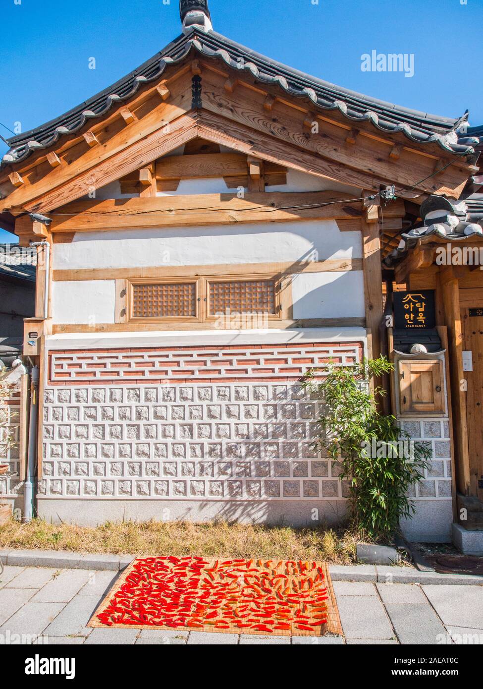 Peperoncini rossi, di cui fuori ad asciugare al sole, sul tappeto di canna, sulla strada, al di fuori della tradizionale casa hanok, Tongin Mercato, Seoul, Corea del Sud Foto Stock