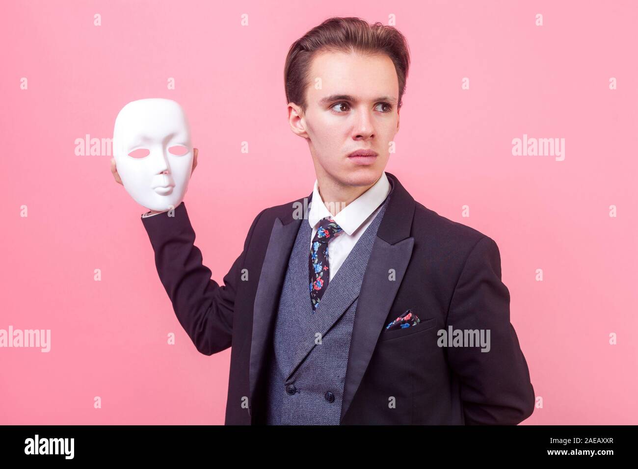 Ritratto di insoddisfazione grave imprenditore nel vestito elegante con il taglio di capelli tenendo maschera bianca, guardando a parte con espressione cupa, personalità multiple. i Foto Stock