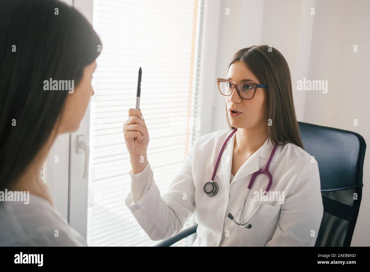 Giovani donne medico esaminando un occhio del paziente riflessi Foto Stock
