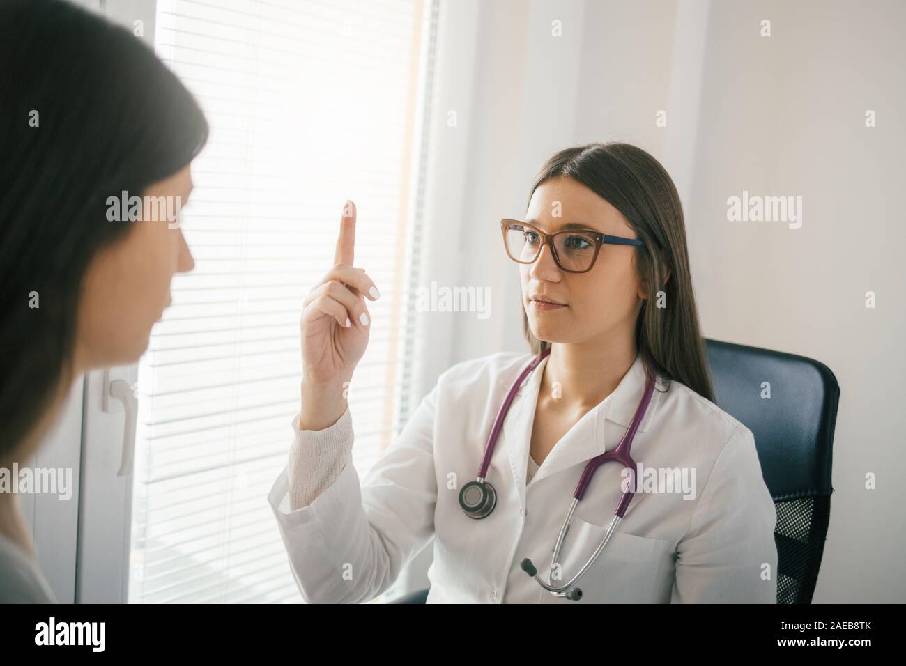 Giovani donne medico esaminando un occhio del paziente riflessi Foto Stock