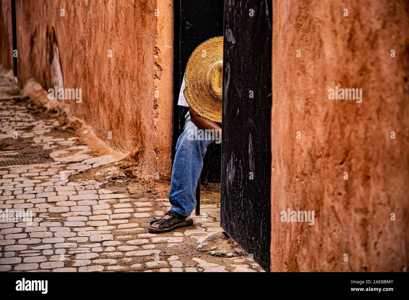 Un uomo del posticipo con un grande cappello di paglia sulla sua testa nella caratteristica stretta strada di terracotta nella Medina di Marrakech Foto Stock