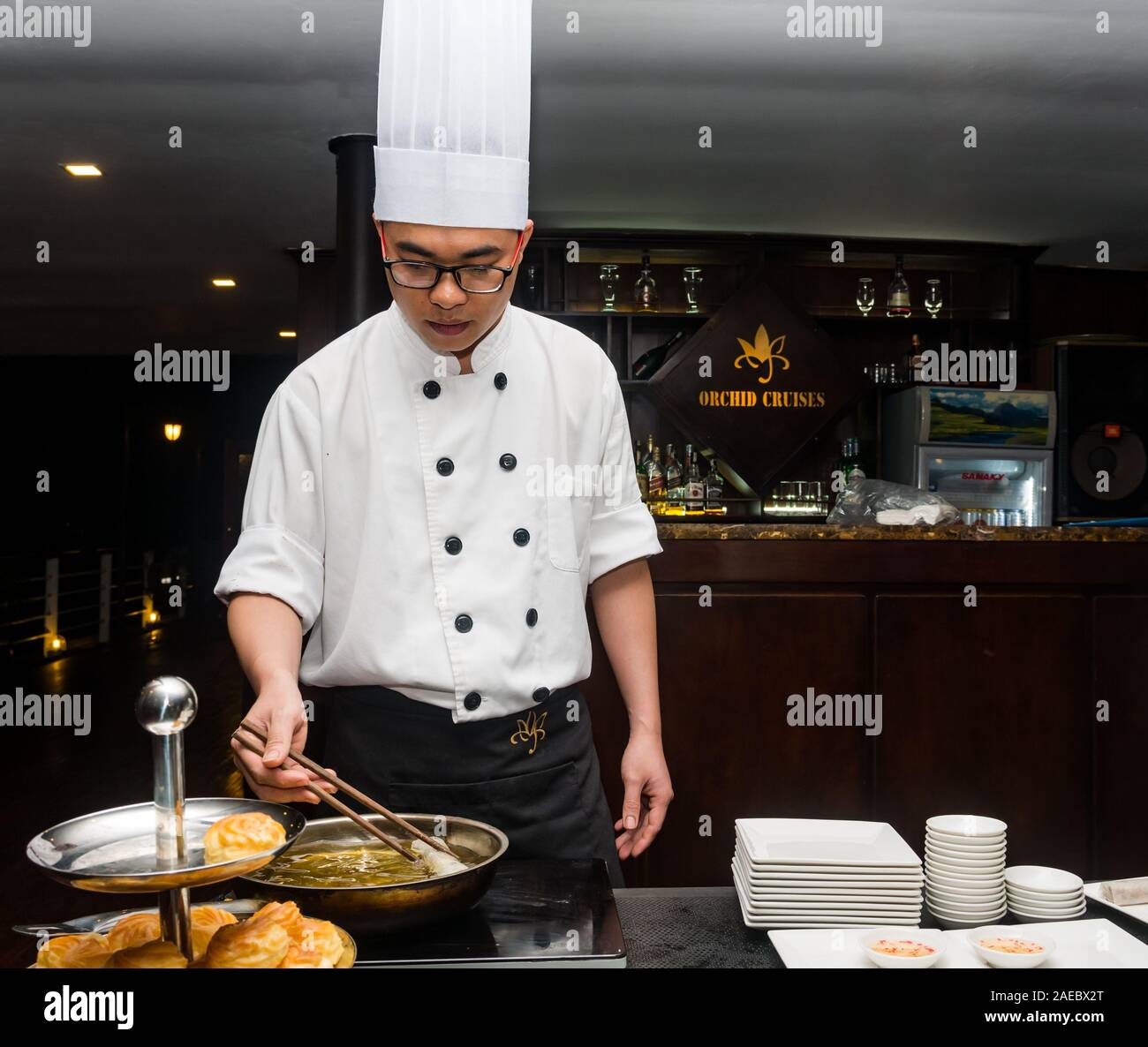 Chef vietnamita che indossa chef bianchi e toque che cucinano involtini primaverili sulla nave da crociera, Vietnam Foto Stock