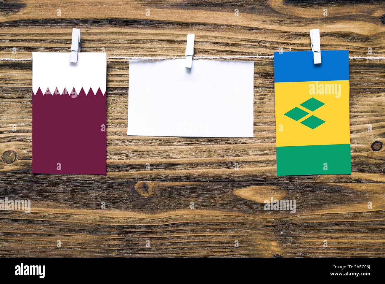 Appendere bandiere di Qatar e Saint Vincent e Grenadine attaccata alla corda con vestiti perni con copia spazio sulla nota di colore bianco su carta backgroun in legno Foto Stock
